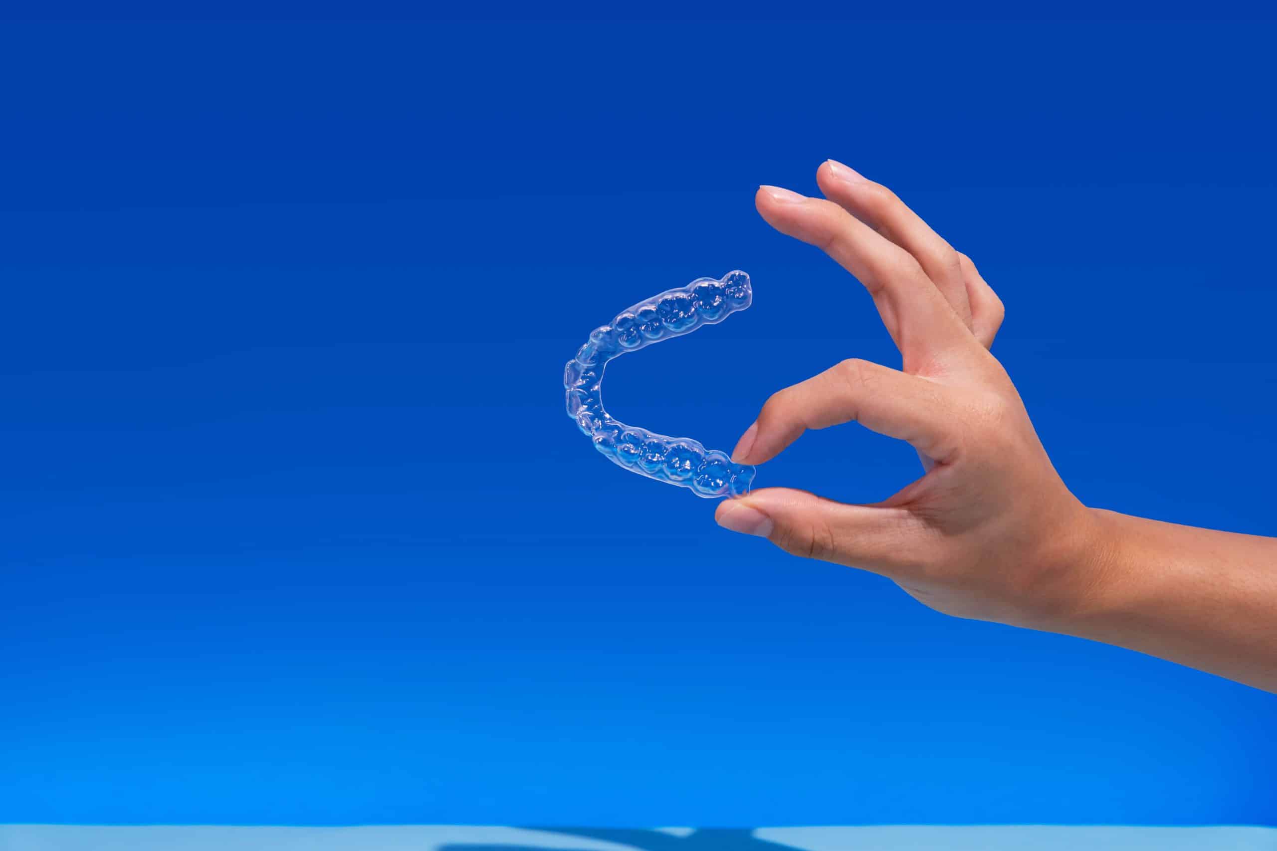 Hand holding Zenyum Clear Aligners over a blue background