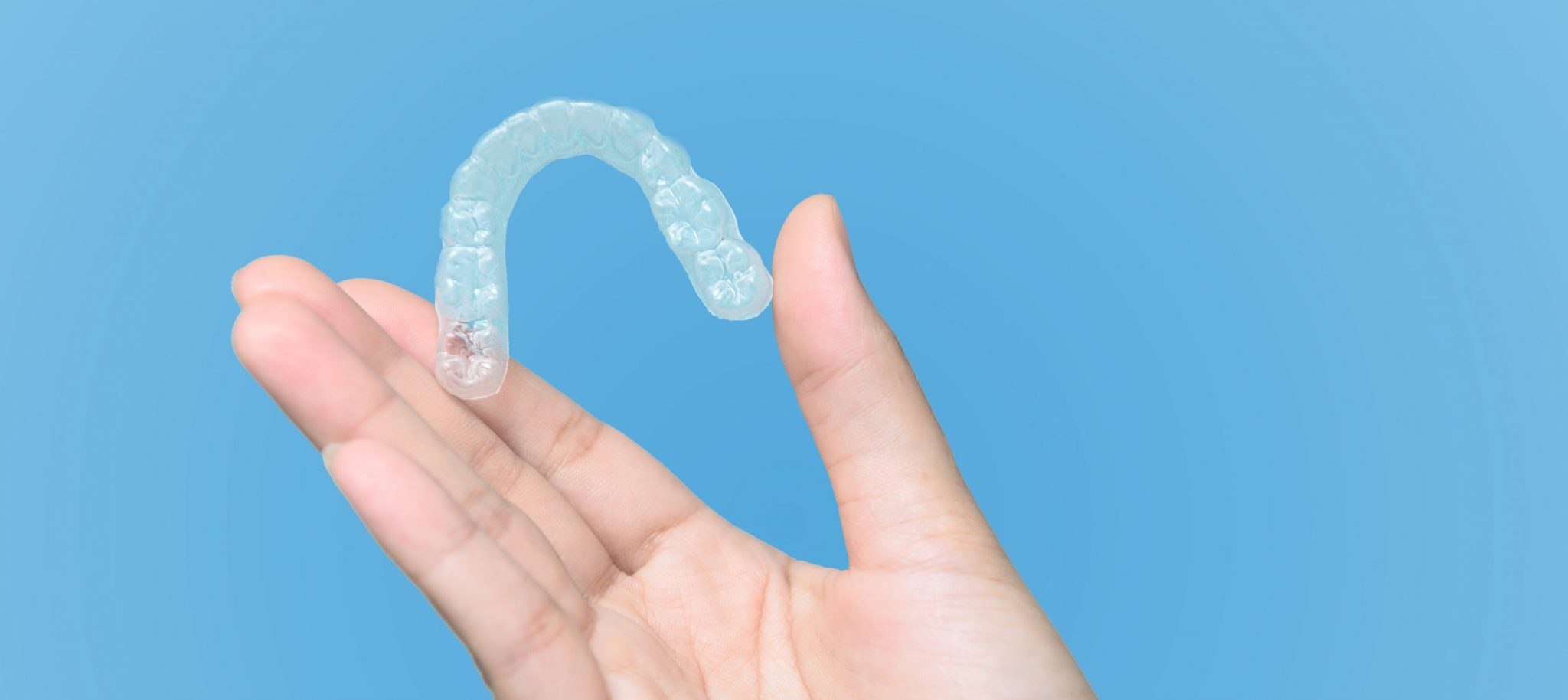 A hand holding up clear aligners