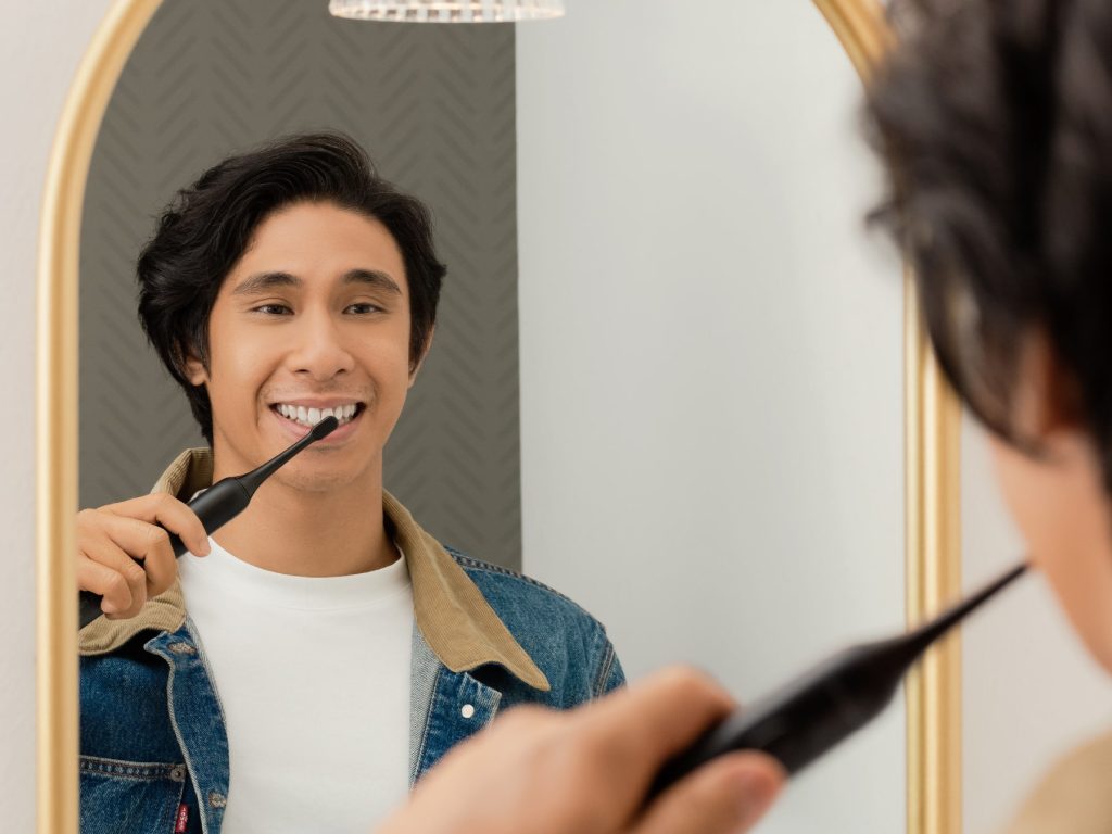 Man looking in a mirror brushing his teeth with electric toothbrush